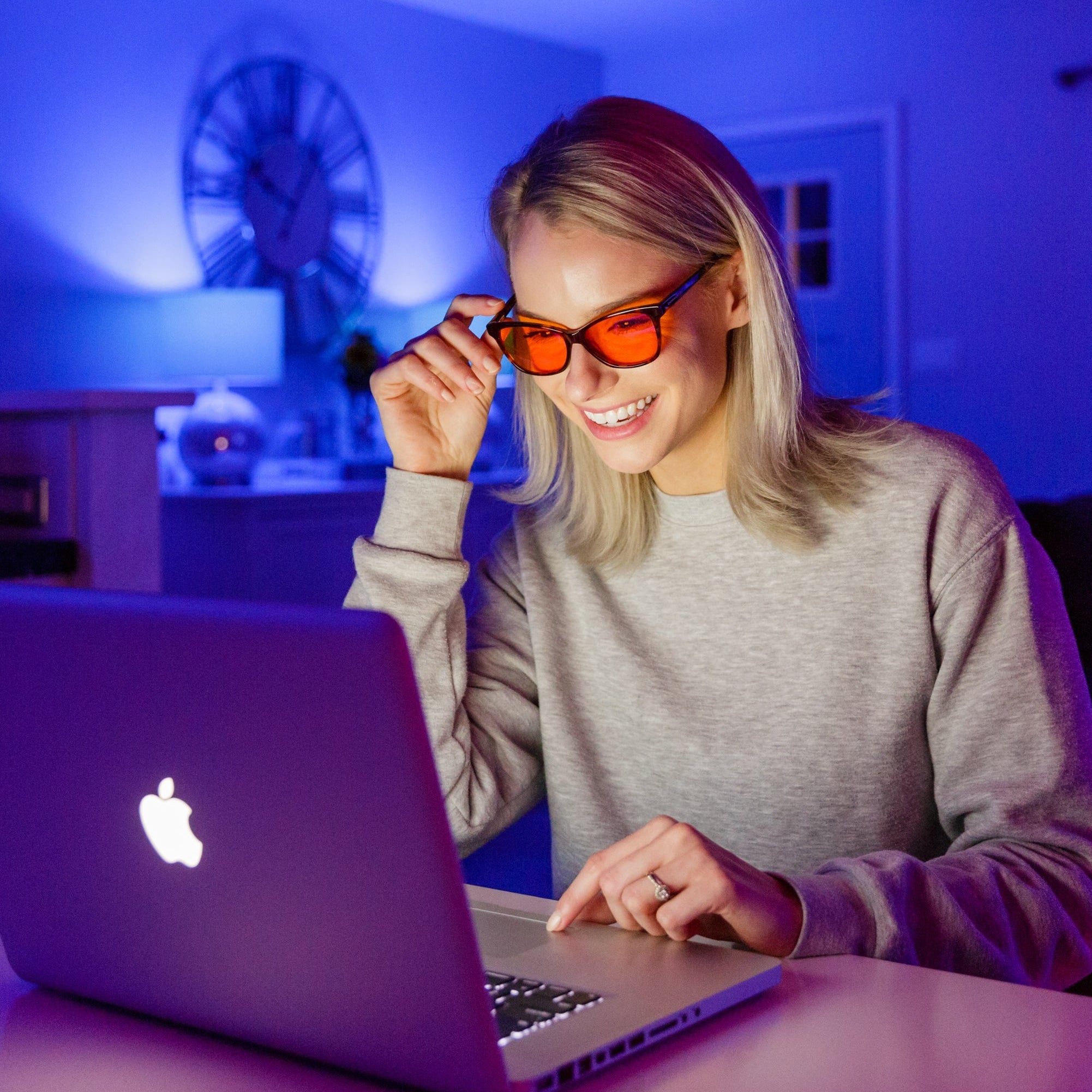 Woman wearing blue-light blocking glasses using a laptop in a dimly lit room with blue lighting.