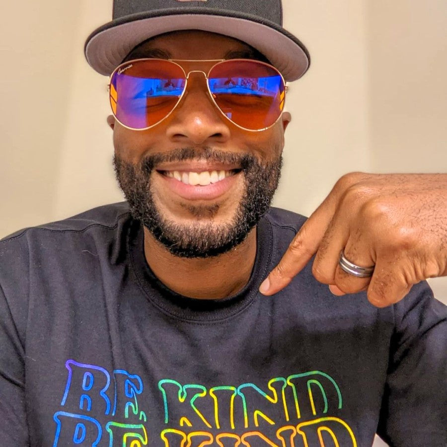 Man wearing sunglasses and a cap, with 'Be Kind' text on shirt