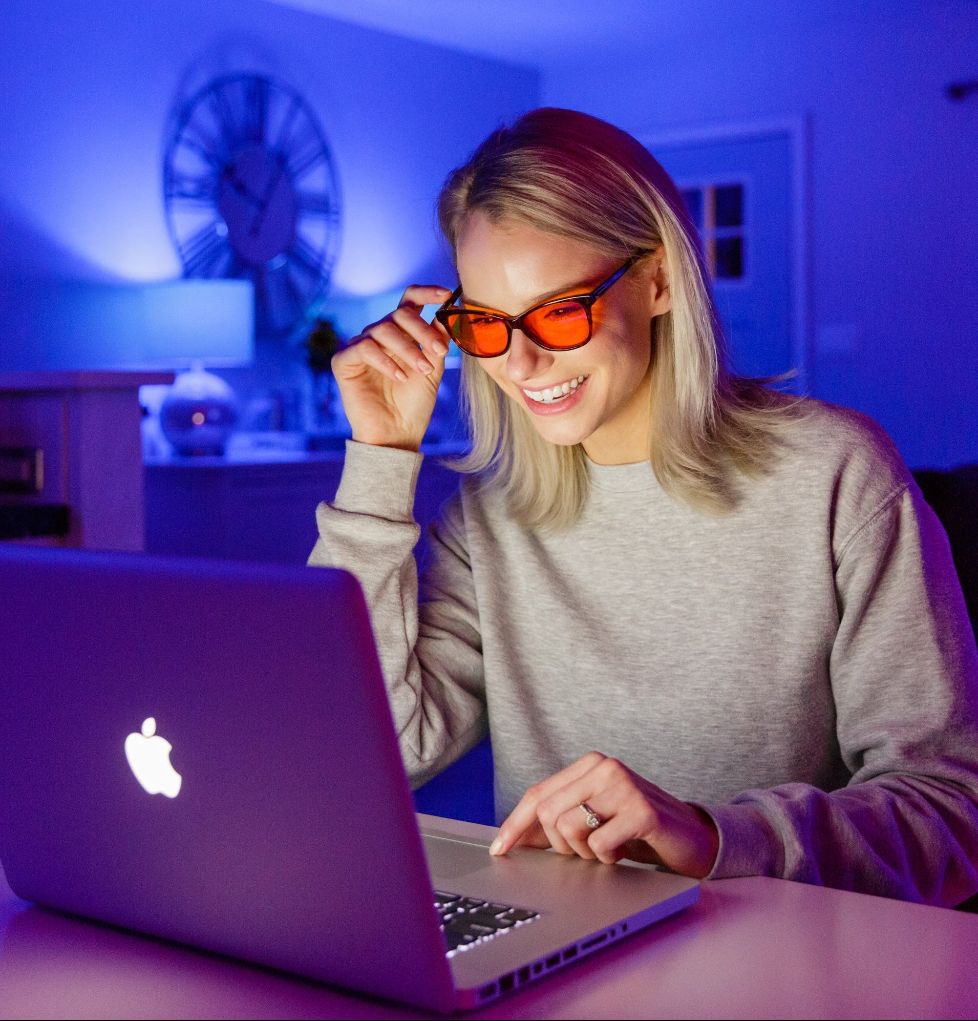 Woman wearing blue-light blocking glasses using a laptop in a dimly lit room with blue lighting.