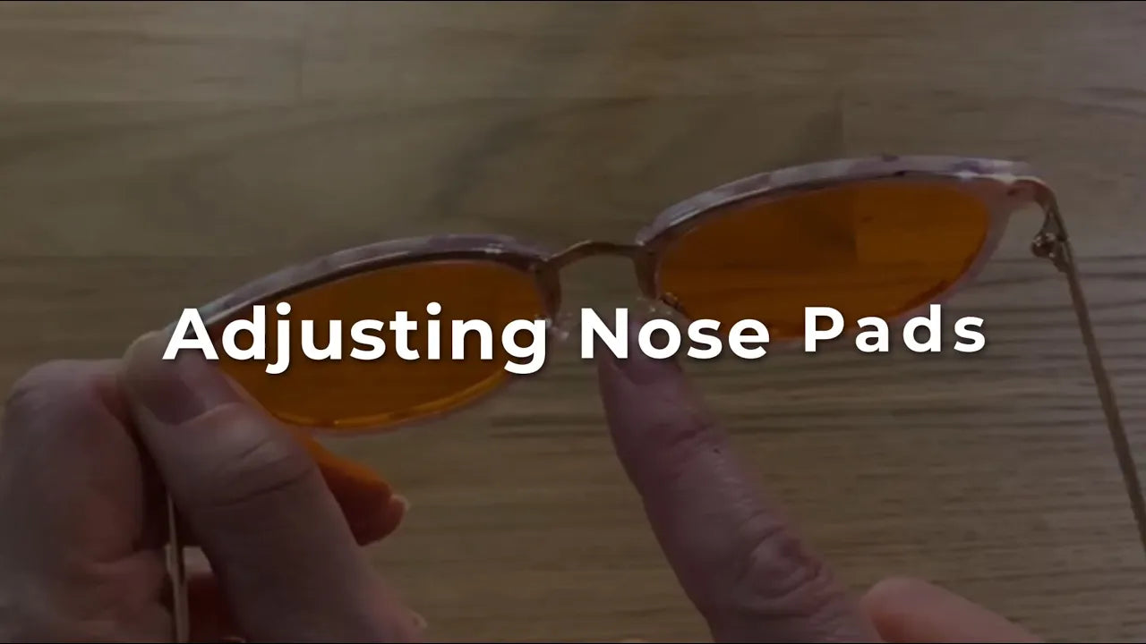 Person adjusting nose pads of sunglasses with text 'Adjusting Nose Pads' on a wooden surface.